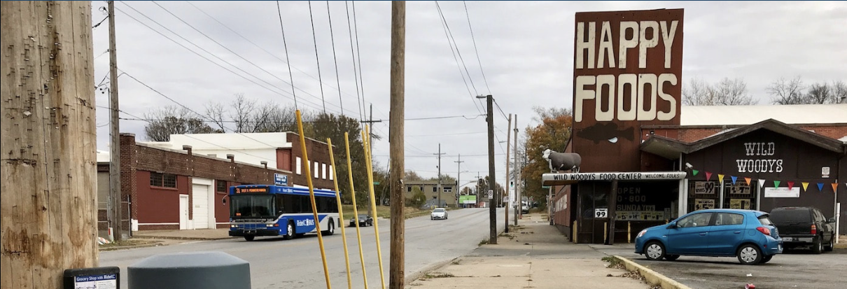 Image of city street with bus and Happy Foods grocery store.